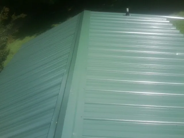 New green metal panels meeting at the ridge of a roof — Flat Roof Repair work by our crew in Sanford